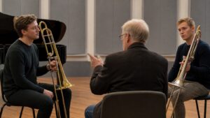 Two trombonists comparing sound concepts in a neutral rehearsal room